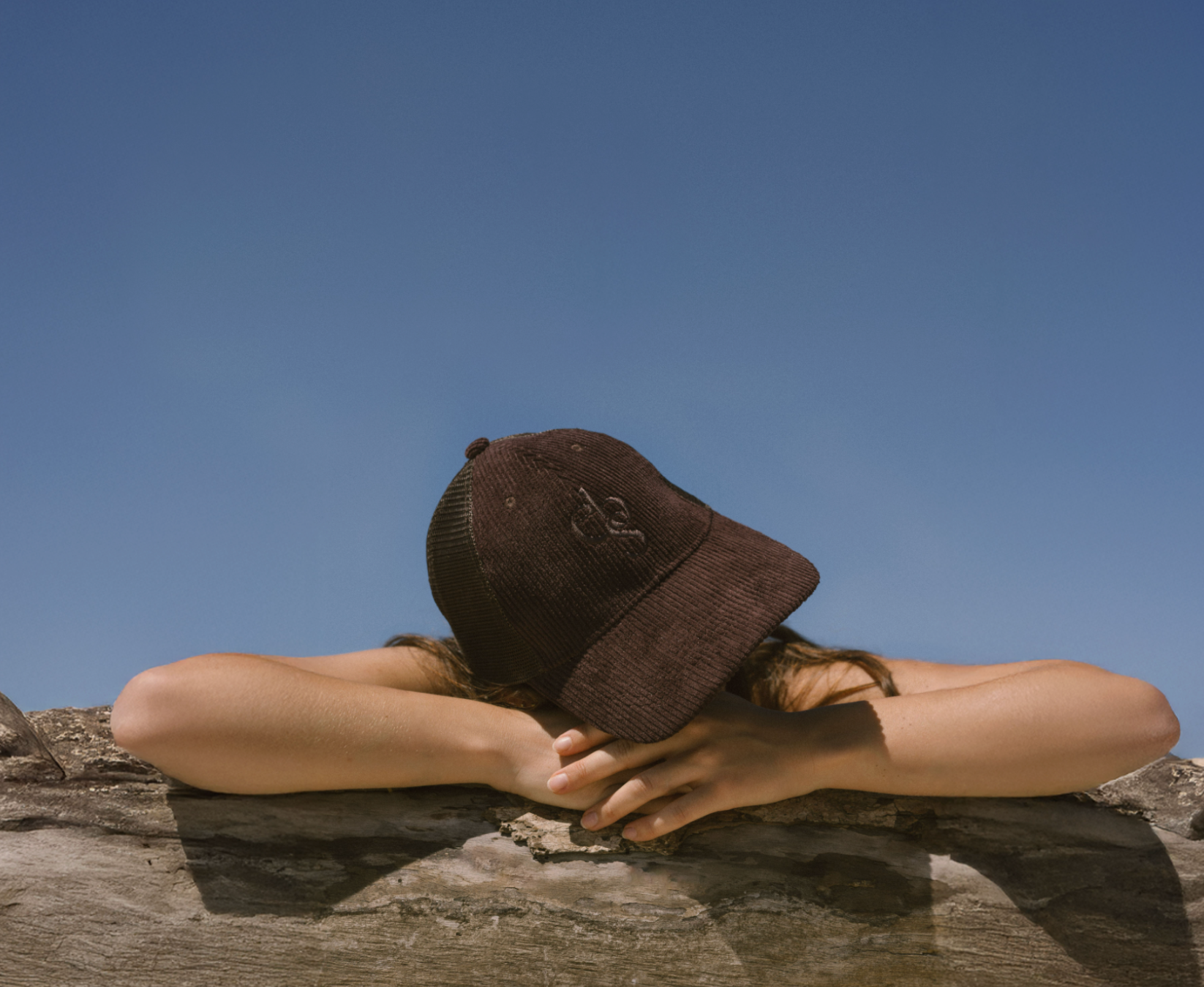 Person wearing Eco By Sonya Good Thoughts Cap on a rock with a clear blue sky in the background