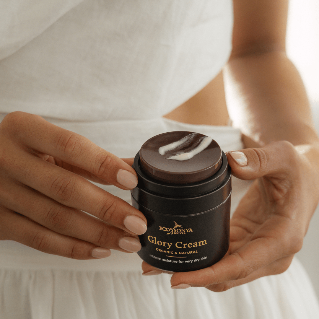 Hands holding Eco By Sonya Glory Cream jar with visible pump and creamy product smear, showing rich smooth texture.