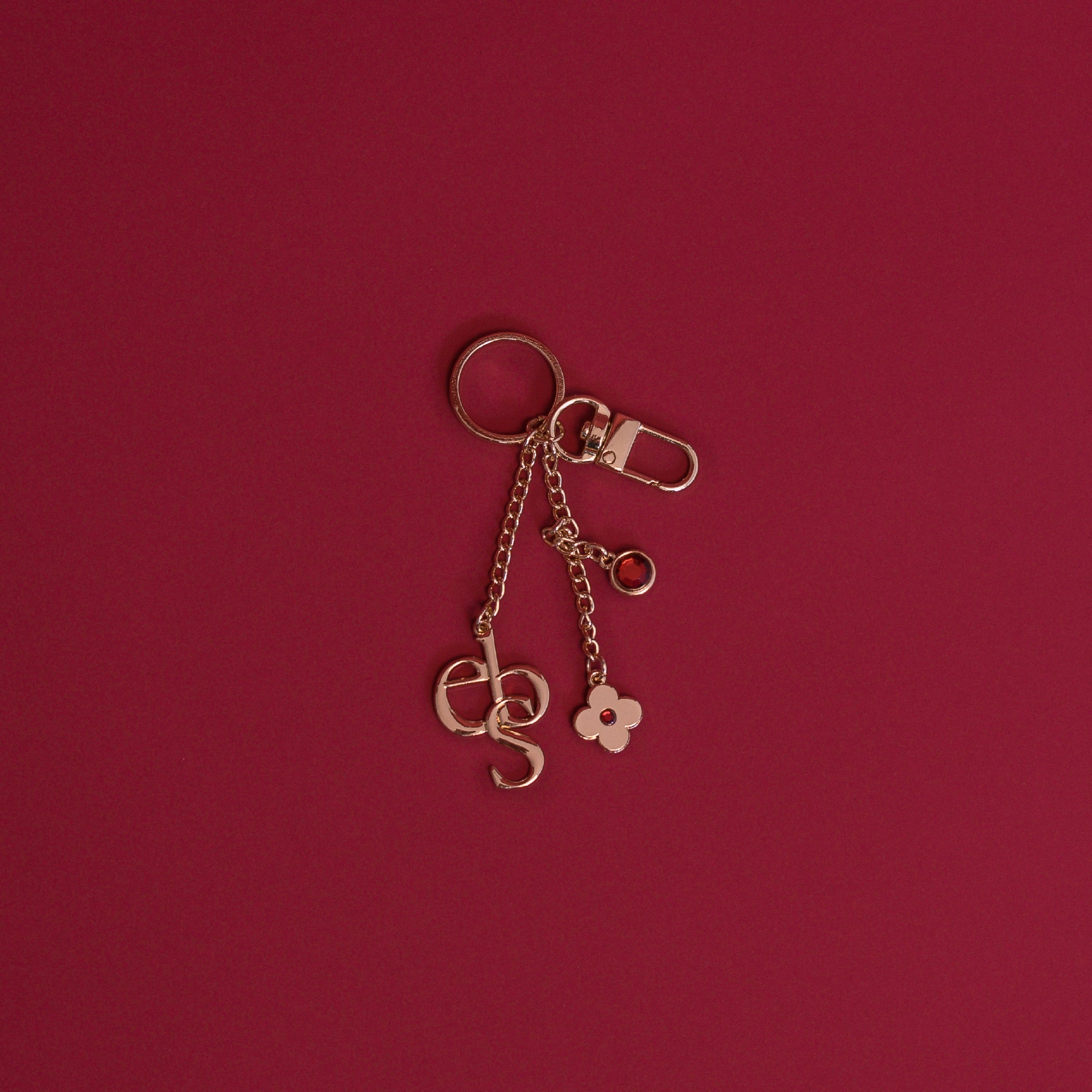 A gold charm keyring on a deep red background.