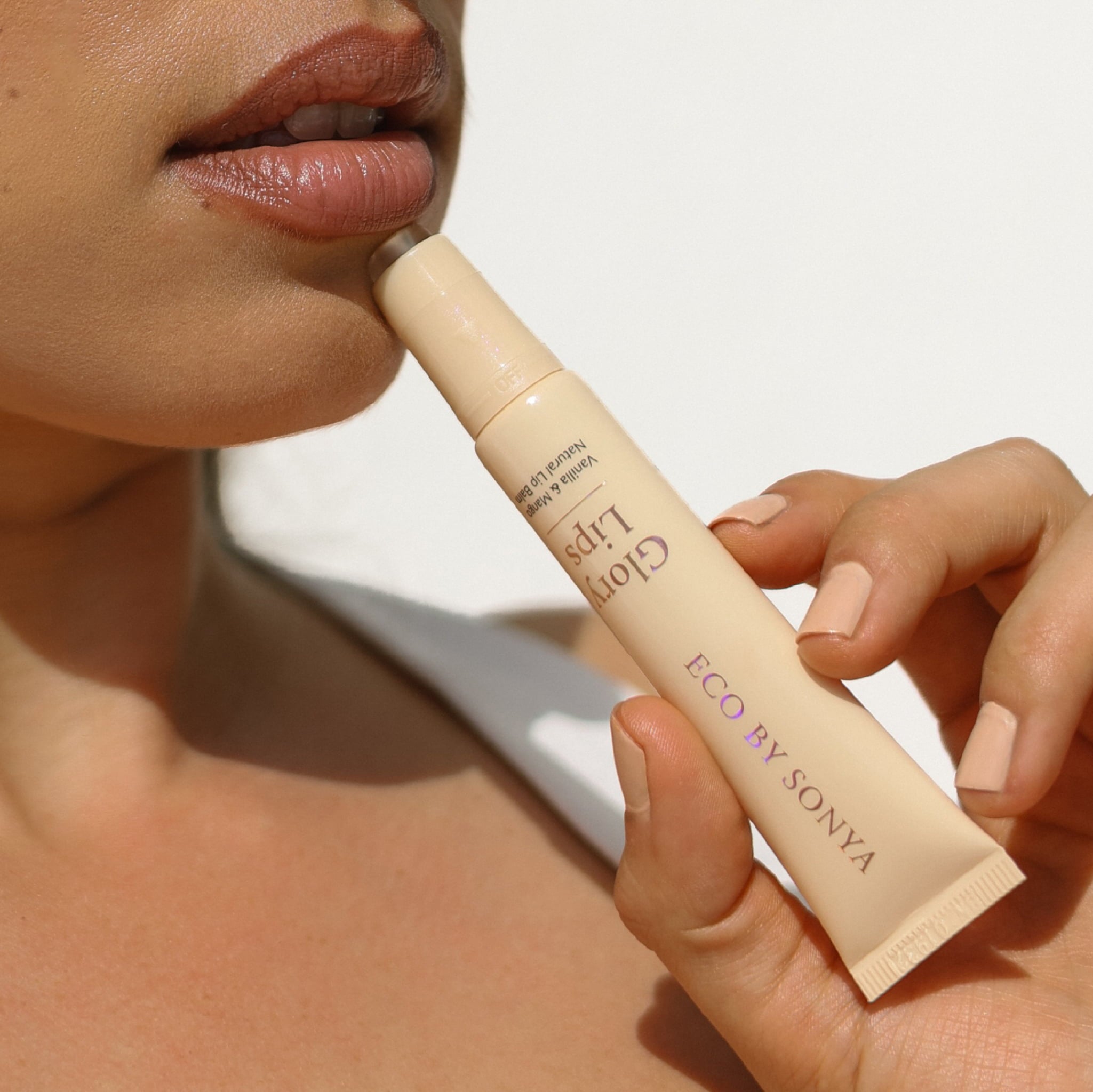 Close-up of a person holding an Eco By Sonya Glory Lips Lip next to their lips, showcasing the product against a clean white background.