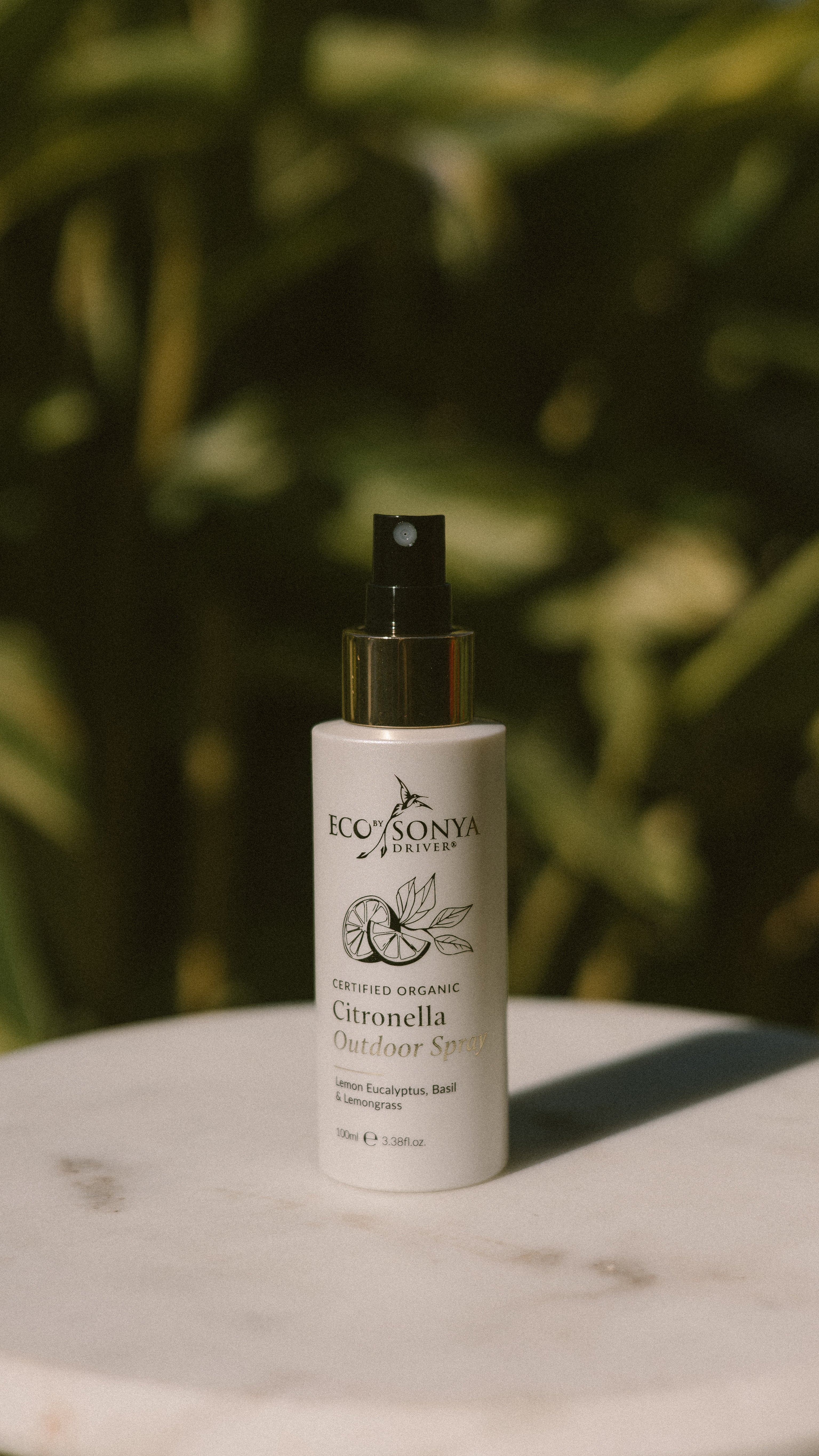 Eco By Sonya Citronella Outdoor Spray on a marble surface with green foliage in the background