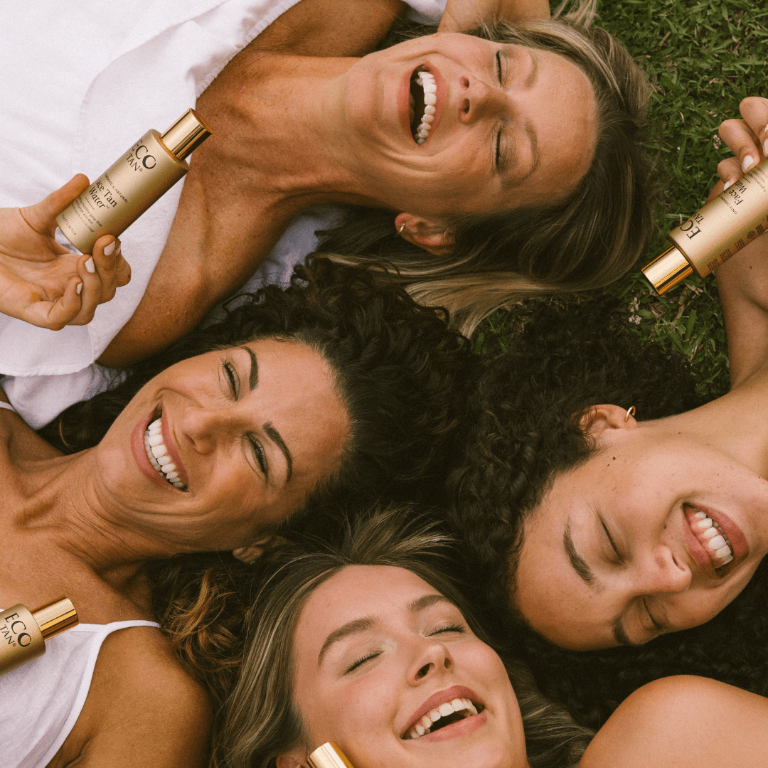 Four smiling women holding Eco Tan Face Tan Water bottles, showing radiant sun-kissed glow in natural sunlight.
