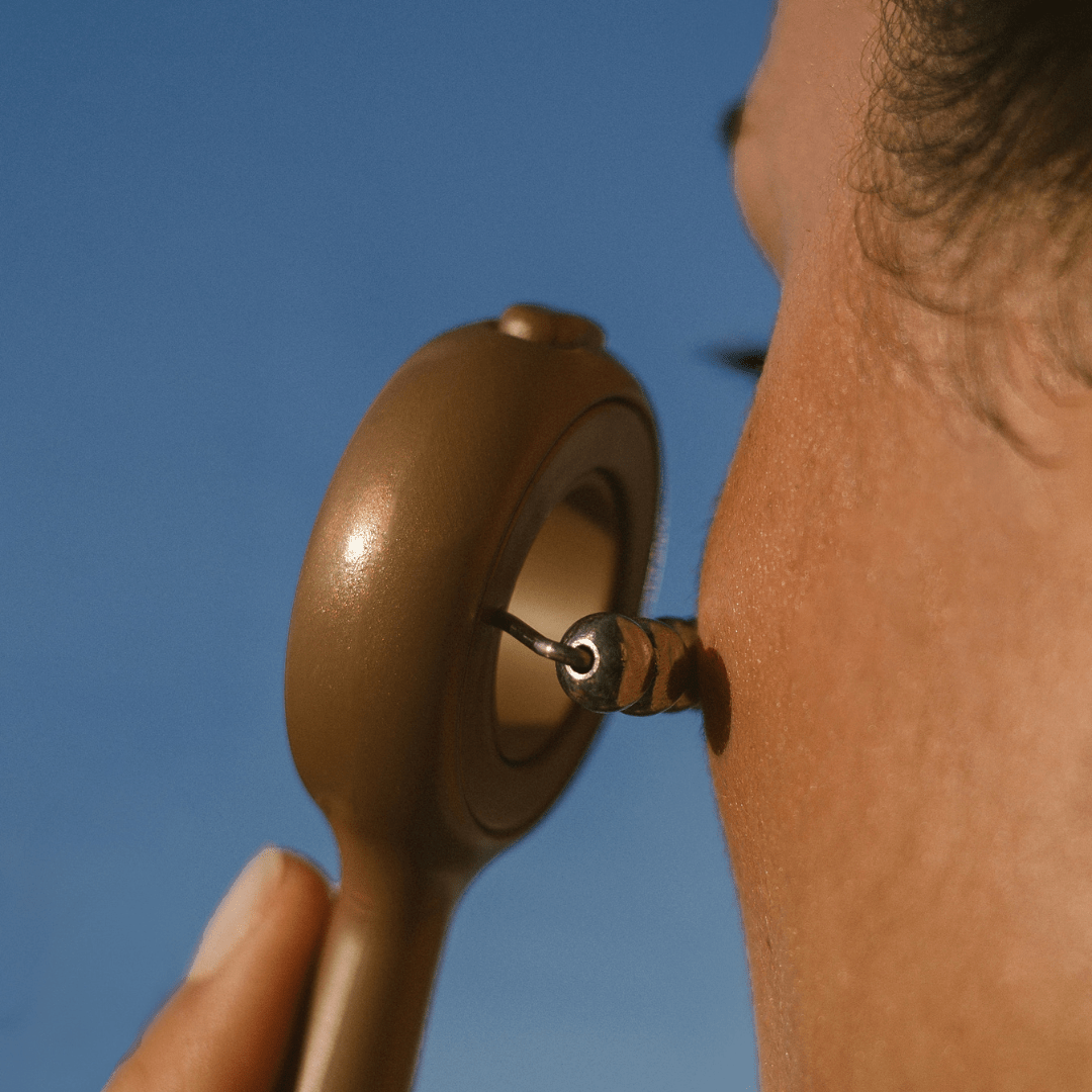 Close-up of a person using face workout sculpting tool against a blue sky.
