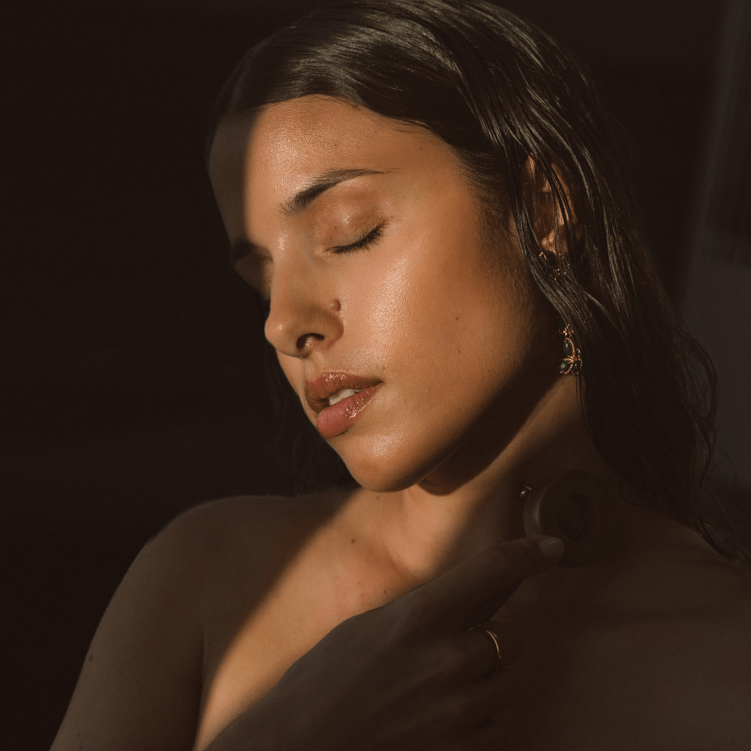 Woman with closed eyes with face workout tool against a dark background