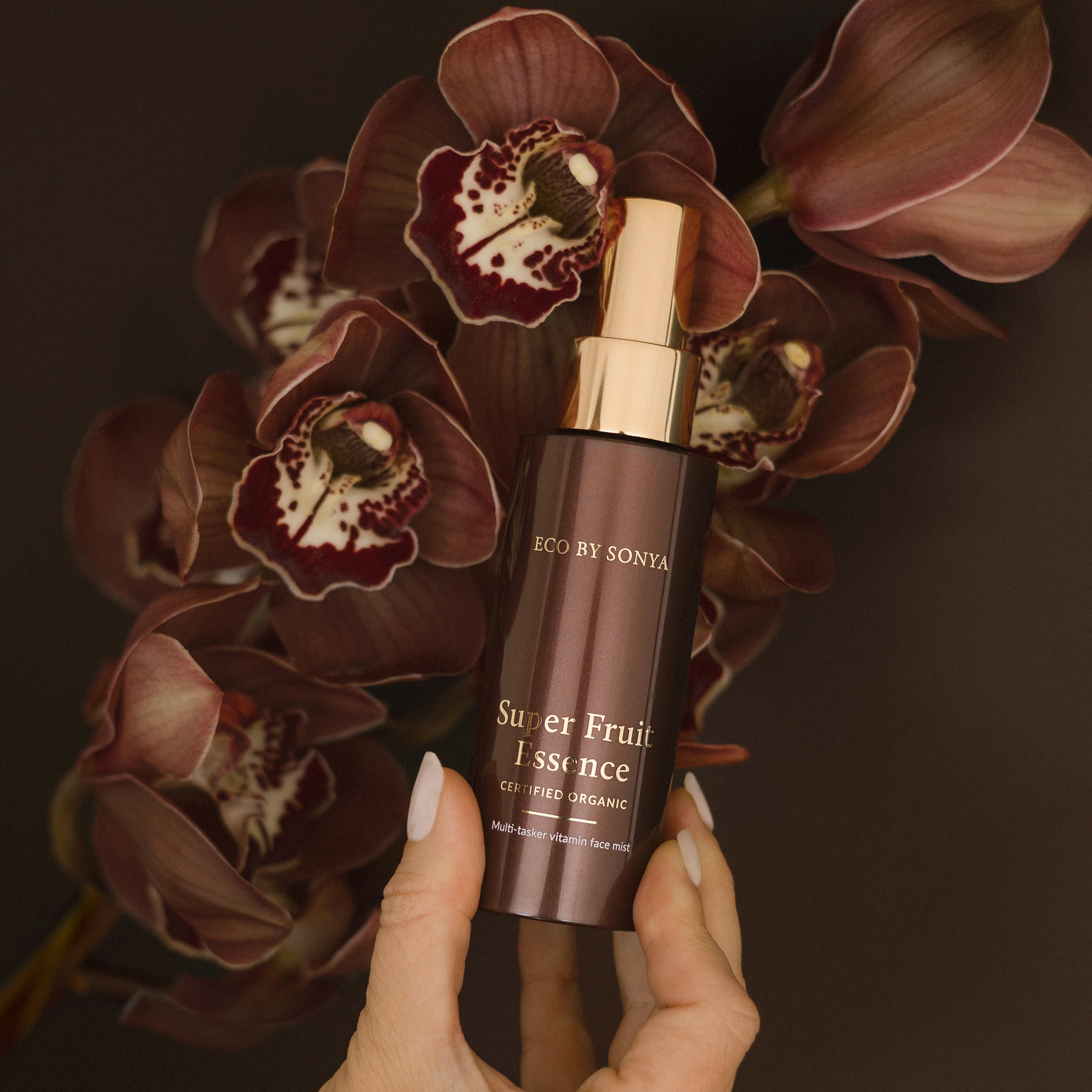 Hand holding a bottle of 'Super Fruit Essence' with dark flowers in the background